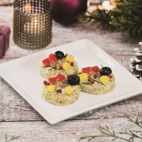 オニギリスタンド ギュッ（onigiri stand Gyu!）によるクリスマスリースをイメージした輪っか状のバジル風味おにぎりに2種類のチーズとオリーブ、パプリカ、ピンクペッパーなどをトッピングした「クリスマスリース風 チーズ＆バジルおにぎり」（税込378円）